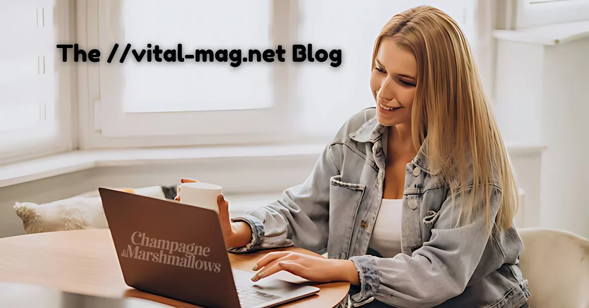 Smiling woman in a denim jacket holding a coffee cup while working on a laptop that displays the words 'Champagne & Marshmallows,' representing her engaged and productive experience with The //vital-mag.net Blog.