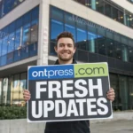 a man holding a "OntPressCom Fresh Updates" sign in front of a building. The building has multiple stories and largewindows. There's a city skyline in the background. The lighting is bright.