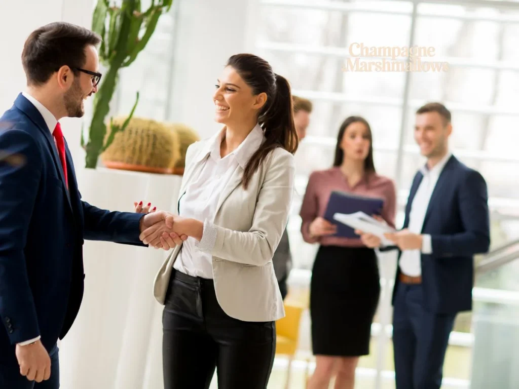 pedrovazpaulo business consultant shaking hands with a client in a bright, modern office, with colleagues engaging in discussion in the background, reflecting a professional and collaborative work environment.