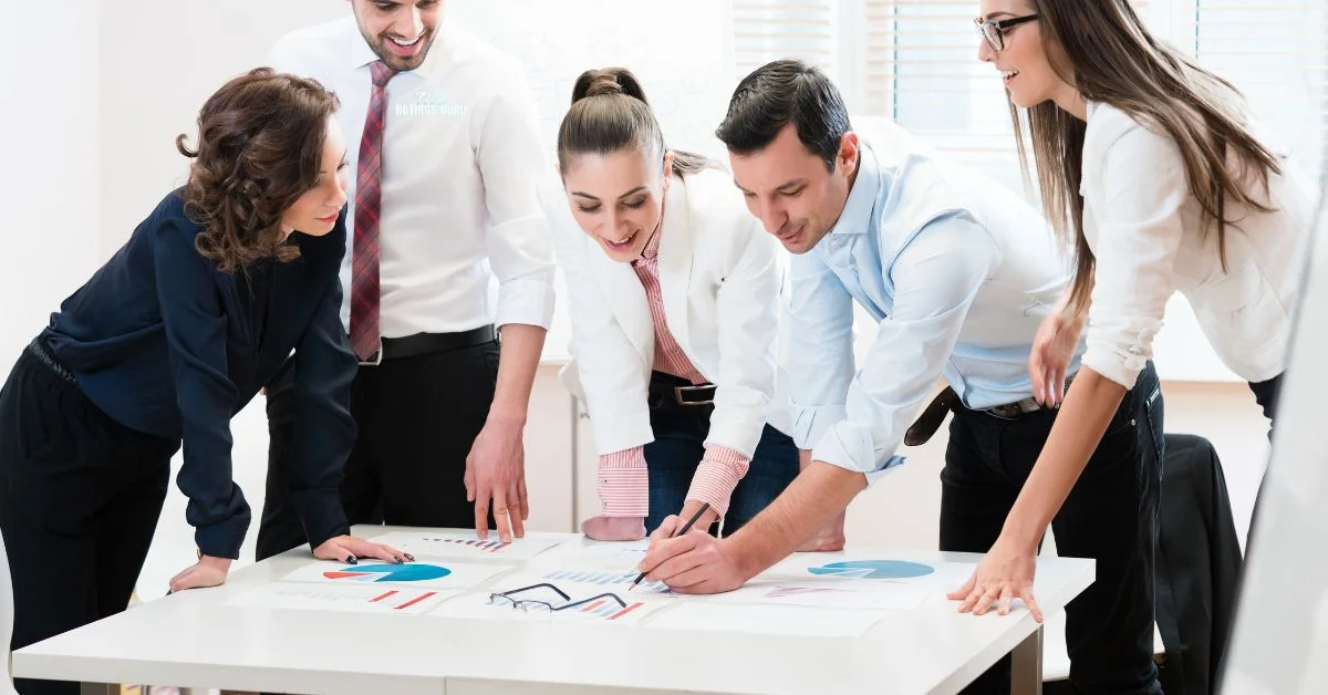 Five professionals, including pedrovazpaulo business consultant, collaborating on business charts and graphs around a table, showcasing teamwork and strategy development in a modern office setting.